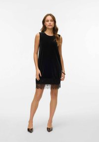Svart ärmlös klänning i sammetstyg, med en spetskant. Designen är löst sittande med en rund halsringning och slutar strax ovanför knäna.