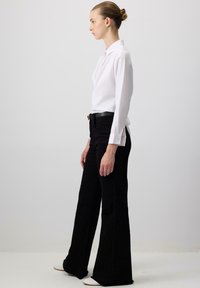 Camicia bianca con bottoni e maniche lunghe, abbinata a pantaloni neri a vita alta e svasati. Design minimalista, tessuto morbido e vestibilità sartoriale.