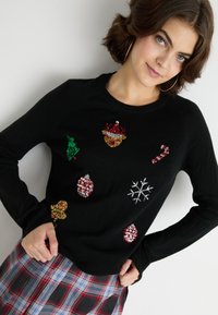 Pulover negru cu aplicații colorate din mărgele: modele de brad de Crăciun, ornamente, baston de zăpadă și fulgi de zăpadă. Mâneci lungi, gât rotund.