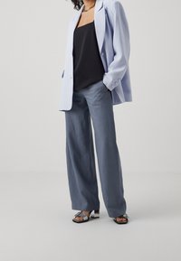 Blazer oversize blu chiaro, canotta nera, pantaloni a gamba larga grigi e sandali con tacco alto argento con dettagli metallici.