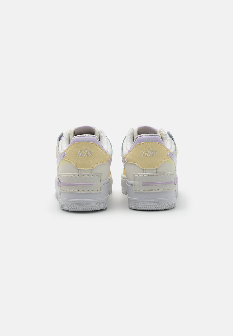 Zapatillas Nike con una base blanca, acentos en amarillo y lavanda, cuero texturizado, cuello acolchado y logotipo en el talón.