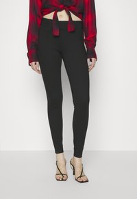 Leggings noirs ajustés en matière extensible, avec une texture lisse et une taille élastique, associés à des talons noirs à lanières.