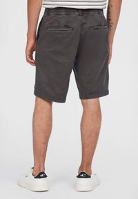 Donkergrijze shorts met een elastische tailleband, twee achterzakken en opgerolde cuffs, gemaakt van een katoenmix. Draagt met witte sneakers.