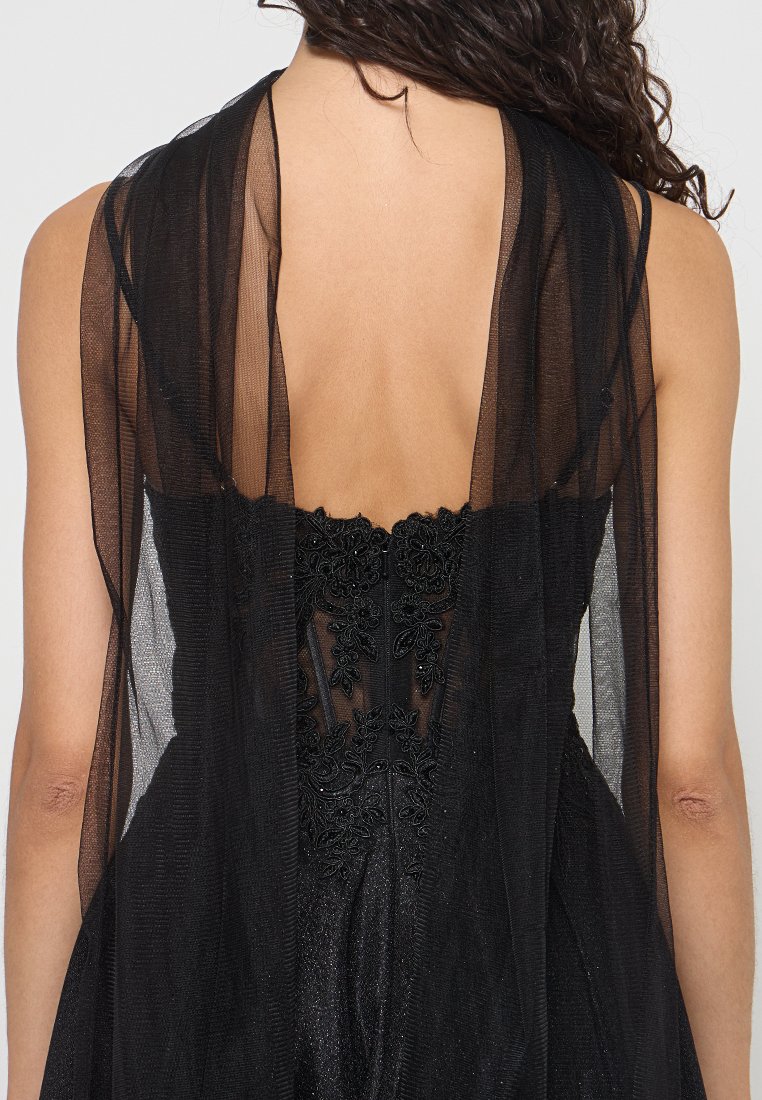 Schwarzes Kleid mit transparenter Überlagerung, das eine aufwendige Blumenstickerei im Oberteil, ein offenes Rückendesign und eine weiche, fließende Textur aufweist.