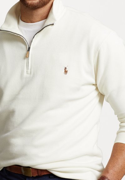Crème fleece pullover met lange mouwen, een rits tot een kwart en een klein geborduurd logo op de borst. Bevat ribbeltextuur en vlakke naden.
