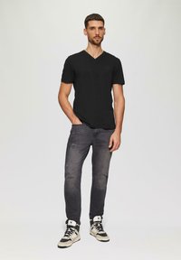 T-shirt nera a scollo a V, jeans grigi scuri strappati e sneakers alte con una combinazione di colori crema e nero. Outfit casual, design attillato.
