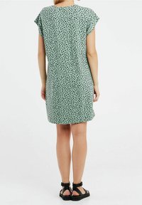 Grön klänning med korta ärmar och svart prickmönster, knälång, i slätt tyg och med avslappnad passform, parat med svarta sandaler.