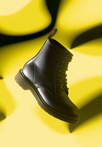 Bottine en cuir noir avec une texture lisse, bout rond et surpiqûres jaunes contrastantes. Elle est dotée de lacets et d'une languette.