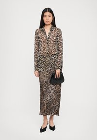 Leopard print dress with long sleeves, buttoned collar, and transparent fabric. Worn with black accent handbag and pointed black shoes.