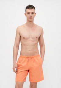 Lys orange svøm shorts lavet af letvægtsmateriale, med en elastisk talje med snor og en diskret logo detalje på kanten.
