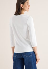 Witte top met 3/4 mouwen van zachte katoen, met een ronde halslijn. Gedragen met blauwe spijkerbroeken, wat een eenvoudige en cleane uitstraling geeft.