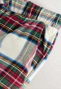Plaid flannel pants in cream, red, green, and blue. Features an elastic waistband, soft texture, and layered pattern with varying stripe widths.