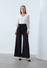 White lace long-sleeve top with a v-neck, paired with high-waisted black wide-leg pants featuring a tied belt. Black stiletto heels.