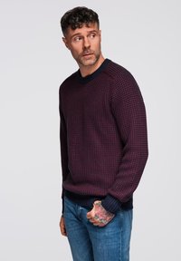 Neulepaita tummanpunaisena ja laivastonsinisenä, jossa on teksturoitu kuvio ja ribbireunukset, lievästi pudotetut olkapäät ja pyöreä kaula-aukko.