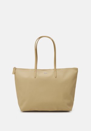 Sac cabas beige avec deux anses, une fermeture éclair et un petit logo sur le devant, présenté sur un fond blanc uni.