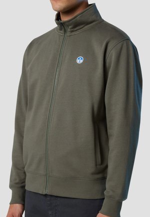 Olivgrüne Reißverschlussjacke aus weichem Stoff, mit hohem Kragen, zwei Seitentaschen und einem runden Logo auf der linken Brust.
