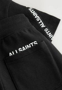 Schwarze Jogginghosen aus Baumwolle mit einem breiten Bund. Verfügen über eine Gesäßtasche und weißen "ALL SAINTS"-Schriftzug an der Seite. Weiche Textur.