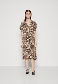 Robe à imprimé léopard en tissu léger, avec un design croisé, des manches courtes et une longueur genou. Portée avec des chaussures noires.