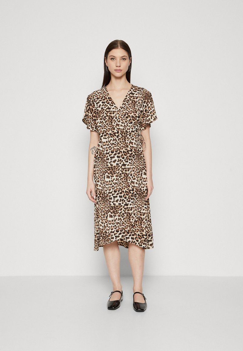 Robe à imprimé léopard en tissu léger, avec un design croisé, des manches courtes et une longueur genou. Portée avec des chaussures noires.