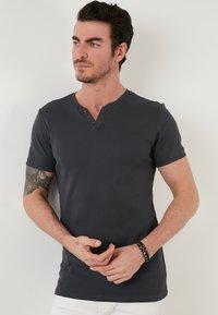 Tricou scurt cu maneci, de culoare gri închis, cu decolteu în V și trei accente cu nasturi maro, realizat dintr-un material neted, cu un design ajustat și fără modele vizibile.