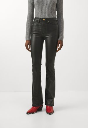 Pantalons évasés en simili cuir noir avec taille haute, dotés de quincaillerie dorée et d'une texture lisse et brillante. Associés à des bottines rouges.