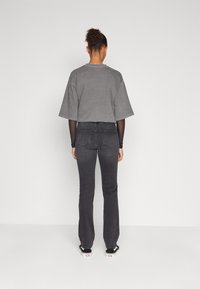 Camiseta gris corta con mangas sueltas, combinada con jeans oscuros de campana. Zapatillas negras con acentos blancos, vistas desde la parte de atrás.