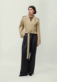 Casaco cropped bege com cintura cingida e mangas largas, emparelhado com calças largas pretas e calçado elegante. Design simples e moderno.