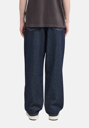 Person wearing dark blue wide-leg jeans, black t-shirt, and white sneakers, shown from the back against a plain background.