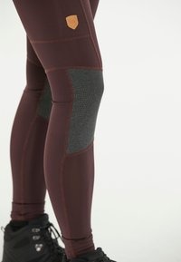 Leggings de sport bourgogne avec un panneau texturé gris au niveau du genou et une petite étiquette logo beige en haut. Tissu lisse et extensible.