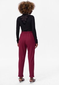 Haut noir à manches longues avec une texture à pois au dos, associé à un pantalon bordeaux fuselé avec une taille élastique et des poignets retroussés.