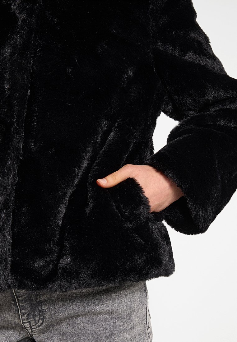 Schwarze Kunstfelljacke mit einer weichen Textur, weiten Ärmeln und seitlichen Taschen. Das Material wirkt dick und gemütlich.