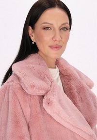 Blød lyserød faux fur frakke med en bred krave og tekstureret overflade. Har store, runde klapper og en afslappet pasform.