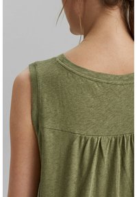 Gros plan sur le dos d'une femme portant un haut sans manches vert olive avec un détail de tissu froncé sous la couture du yoke.