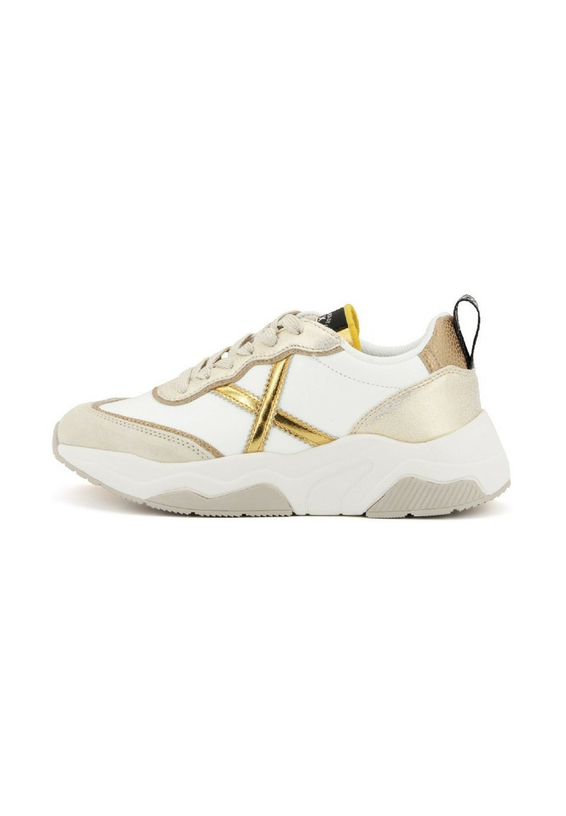 Sneaker bianco e beige con accenti metallici dorati, camoscio testurizzato e una suola bianca spessa. Presenta un tab sulla parte posteriore e lacci frontali.