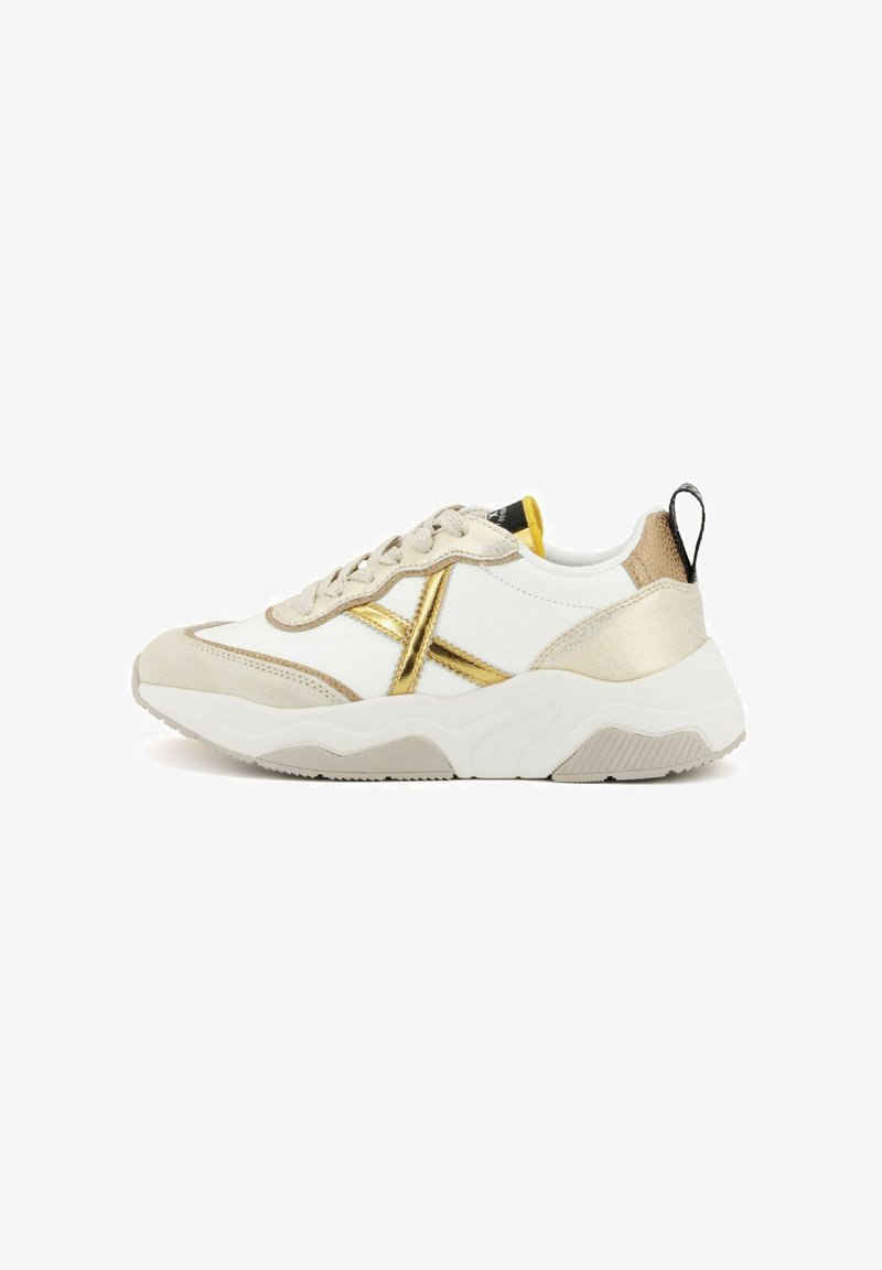 Sneaker bianco e beige con accenti metallici dorati, camoscio testurizzato e una suola bianca spessa. Presenta un tab sulla parte posteriore e lacci frontali.