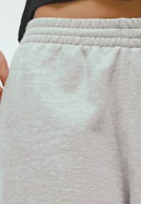 Svijetlosive trenirke napravljene od mekog materijala s elastičnim pojasom, s glatkom teksturom i suptilnim detaljem šivanja duž rubova.