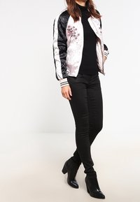 Blouson aviateur noir et argent avec broderie florale, associé à un pull noir et un jean skinny noir. Bottines à talons noires.