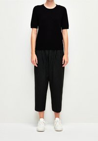 Černý krátký pletený top s krátkým rukávem ve spojení s černými kostkovanými kalhotami 3/4 délky. Outfit doplňují bílé tenisky. Jednoduchý, přiléhavý střih.