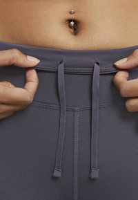 Gros plan sur une paire de leggings violet foncé avec des liens à tirer à la taille et une texture de tissu lisse et extensible.