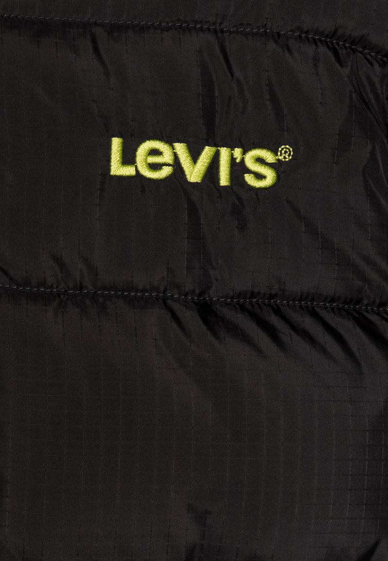 Zwarte gewatteerde pufferjack met een subtiel ruitpatroon, met felgele geborduurde "Levi's"-logo dat prominent zichtbaar is.