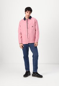 Rosa bomullsjakke med marineblå krage, med frontlommer og trykknap-lukking. Brukt med blå jeans og svarte joggesko.