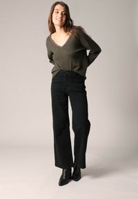 Olijfgroen V-hals sweater met lange mouwen; gecombineerd met hoge taille, wijde zwarte jeans en zwarte enkellaarsjes. Simpel, gestructureerd ontwerp.