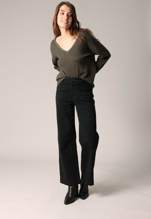 Pull à col V vert olive à manches longues ; associé à un pantalon noir taille haute à jambe large et des bottines noires. Design simple et texturé.