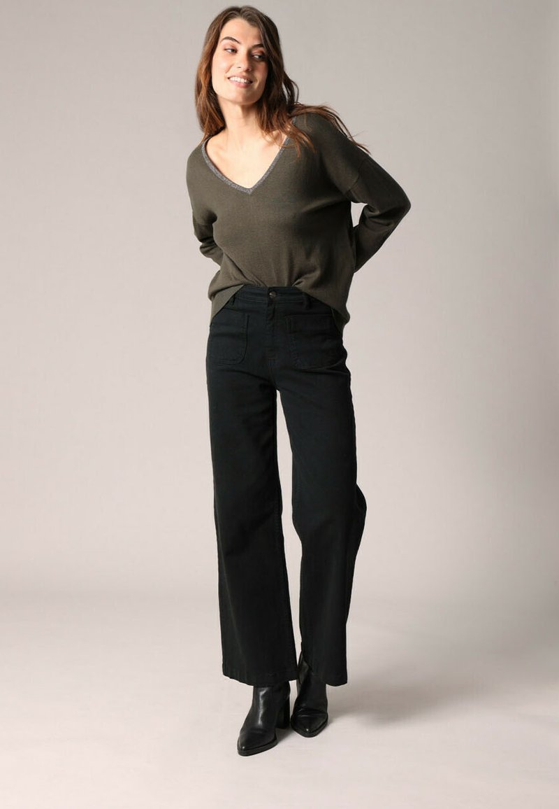 Olijfgroen V-hals sweater met lange mouwen; gecombineerd met hoge taille, wijde zwarte jeans en zwarte enkellaarsjes. Simpel, gestructureerd ontwerp.