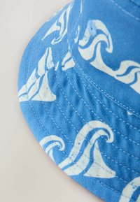 Blauer Bucket Hat mit weißen Wellenmustern, aus Baumwollstoff mit gestickten Details am Rand und einer glatten, strukturierten Oberfläche.