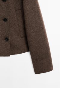 Brun uldfrakke med en skræddersyet design, der har en knaplukning, store knapper og en sidelomme. Blød tekstur med en struktureret ærme.