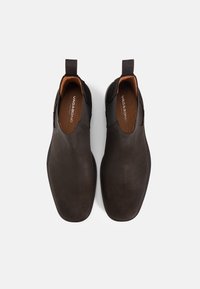 Σκούρα καφέ δερμάτινα παπούτσια που δεν χρειάζονται κορδόνια, με ελαστικές πλαϊνές επενδύσεις, στρογγυλεμένες μύτες και διακριτικές λεπτομέρειες ραφής. Τα επίπεδα πέλματα παρέχουν σταθερή υποστήριξη.