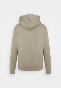 Mikina s kapucí v světlé béžové barvě, měkký materiál, žebrované manžety a lem. Obsahuje šev podél zad a logo na rukávu.