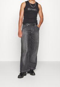 Svart linne med "Crush" i rhinstenar, kombinerat med löst sittande grå denimjeans, avslutat med ett nitar svart bälte och svarta stövlar.