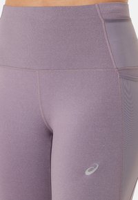 Hochtaillierte, lavendelfarbene Leggings mit einer glatten, dehnbaren Textur, ausgestattet mit tonal abgestimmten Nähten und einem reflektierenden Markenlogo am linken Oberschenkel.
